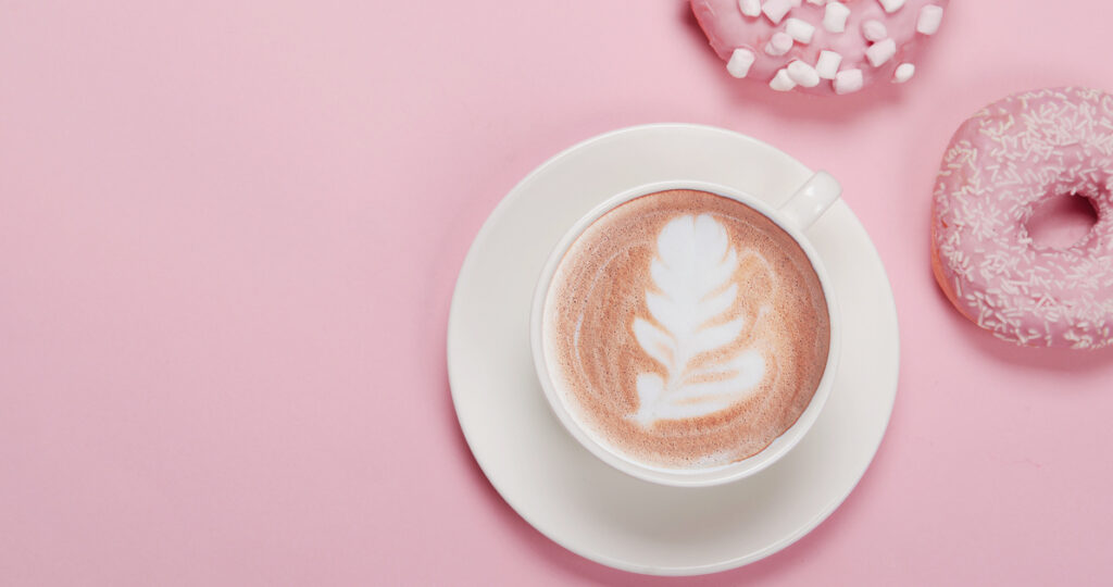 Latte art coffee with pink donuts on table