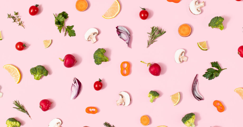 Assorted vegetables and herbs on pink background.