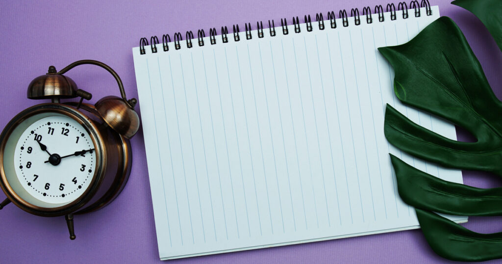 Clock and notebook on purple background with leaves