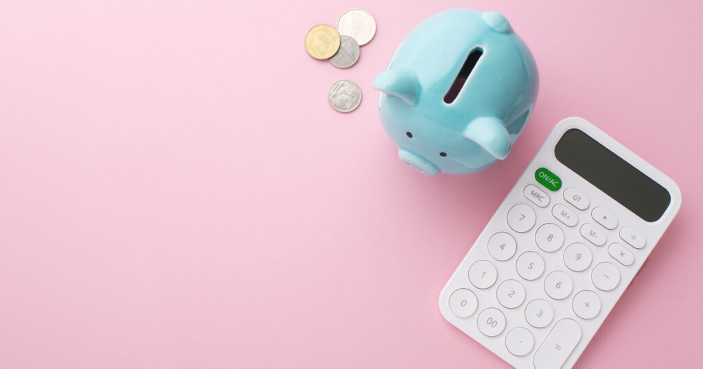 Piggy bank, coins, and calculator on pink background.