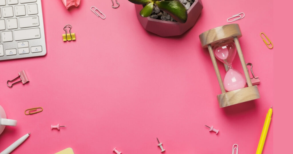 Desk with keyboard, plant, hourglass, pink background