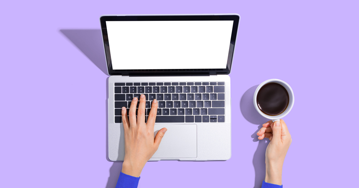 Typing on laptop with coffee on purple background.