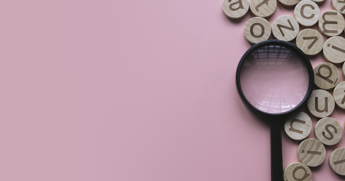 Magnifying glass on letters, pink background.