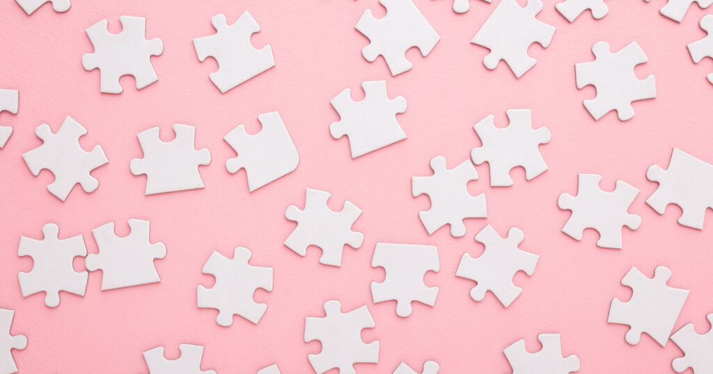 Scattered white puzzle pieces on pink background.