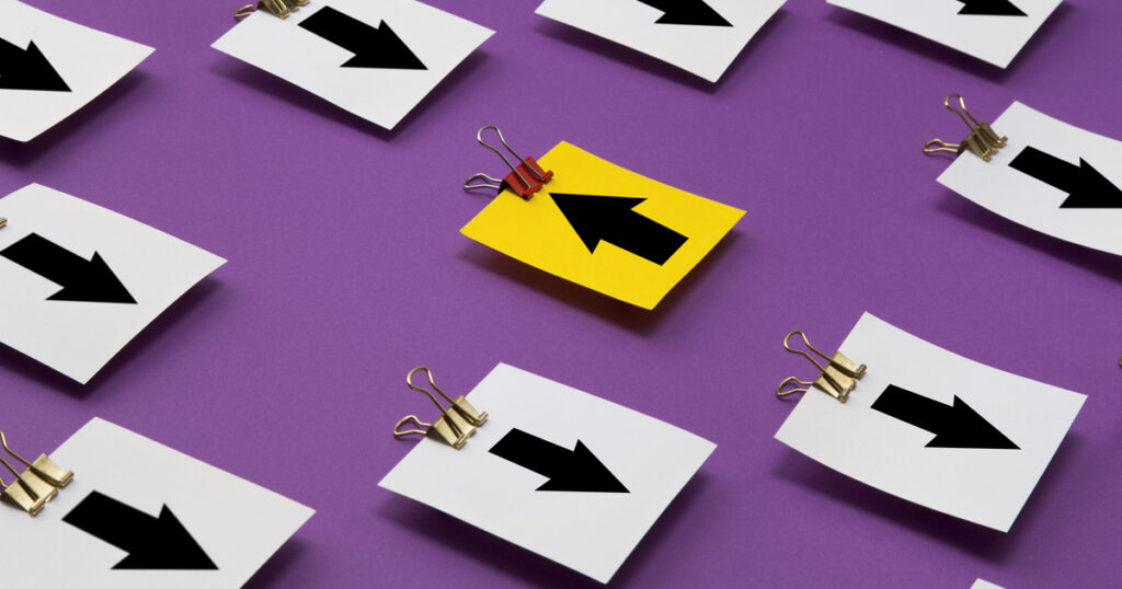 Yellow paper arrow among white arrows on purple surface.