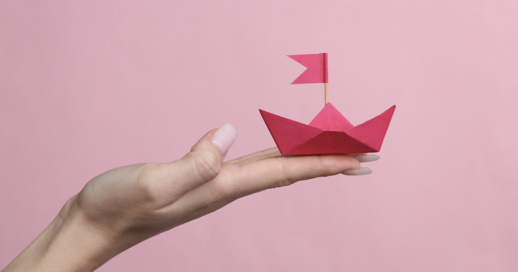 Pink origami boat held on hand.