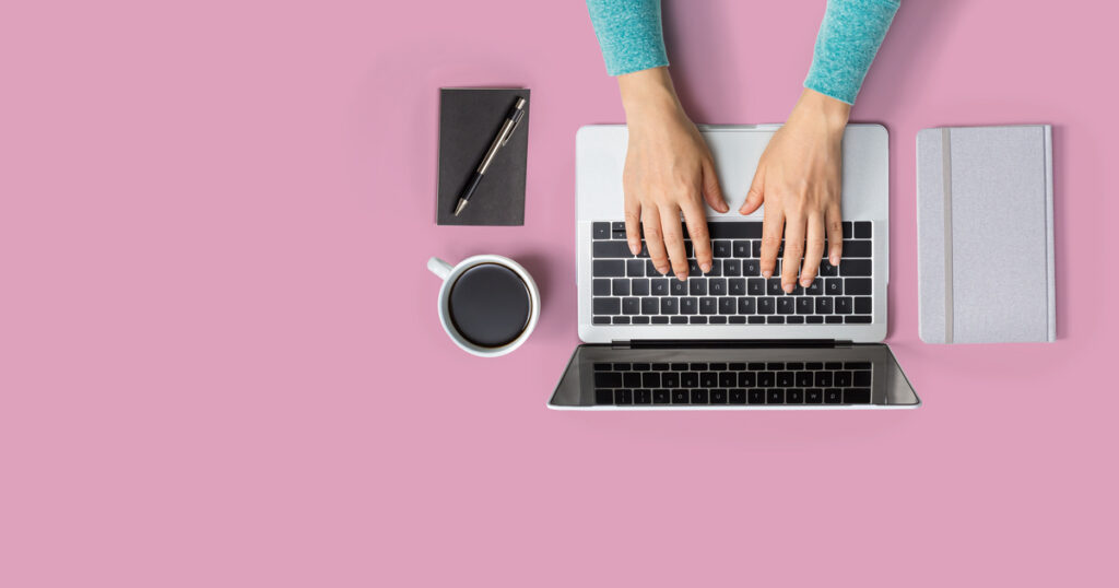 Hands typing on laptop with coffee, notebook