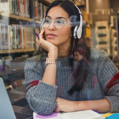 woman wearing headphones while working on her laptop in the library