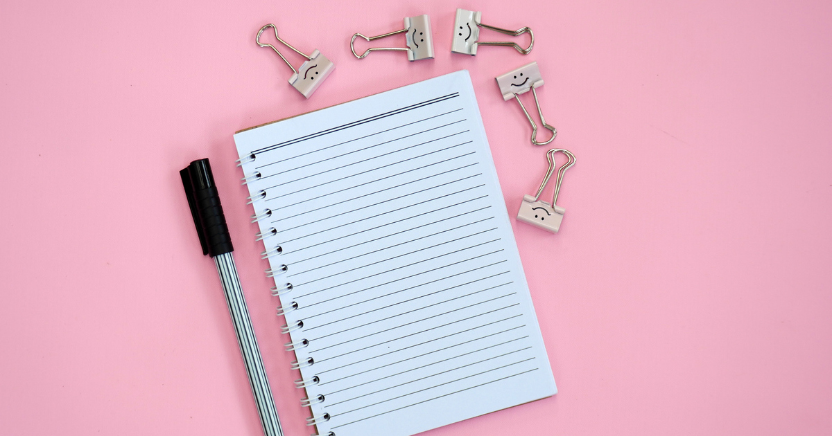 Notebook and pen on pink background with binder clips.