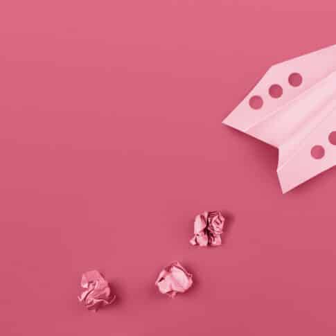 Flat lay of color paper plane colored in trendy color of the year 2023 Viva Magenta