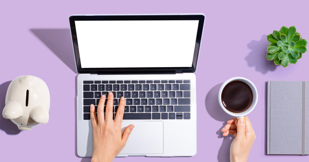 Person using laptop with coffee and plant nearby.