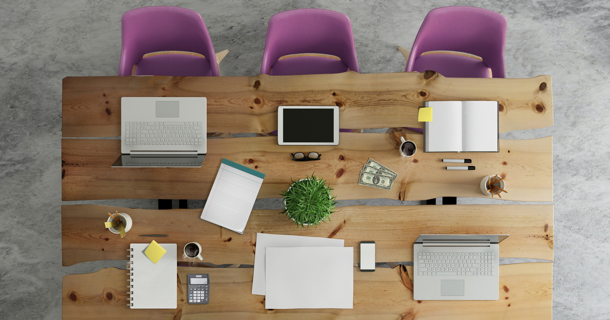 Wooden office desk with laptops, tablet, and stationery.