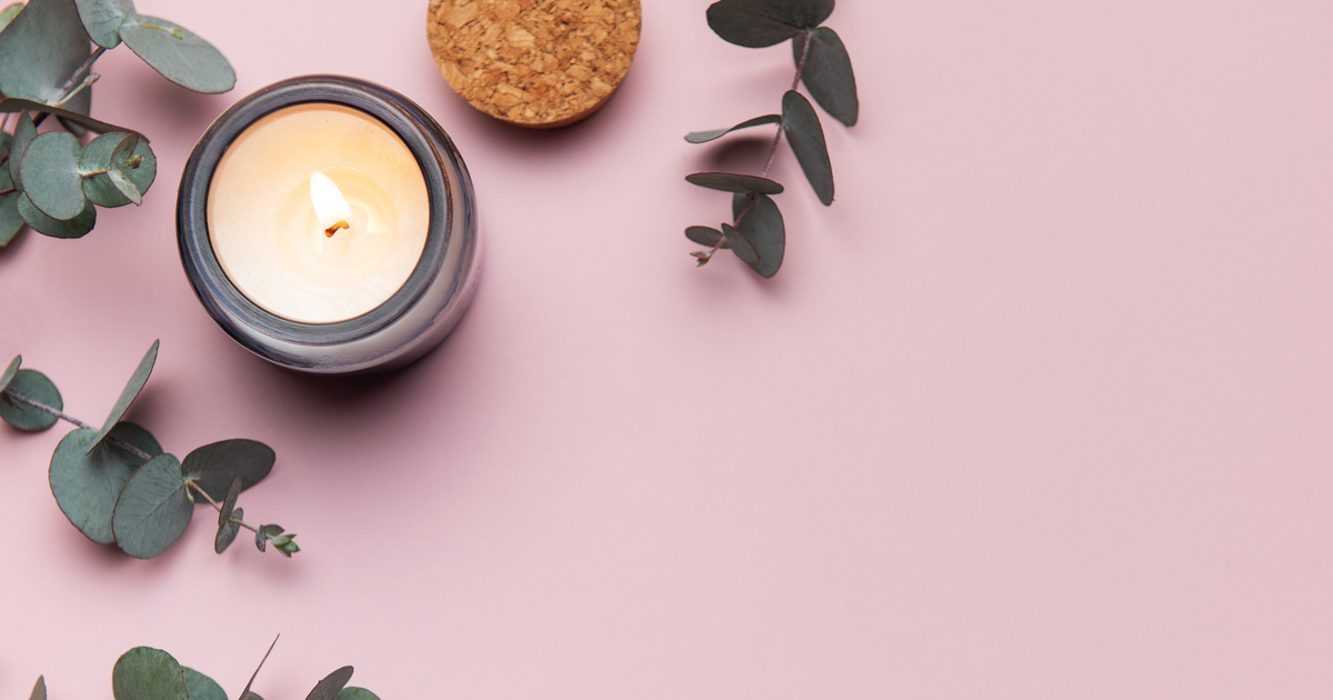 Lit candle with leaves on pink background