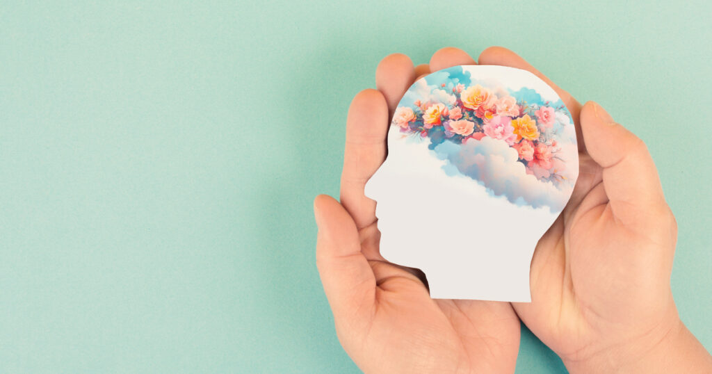 Hands holding head silhouette with flowers inside.