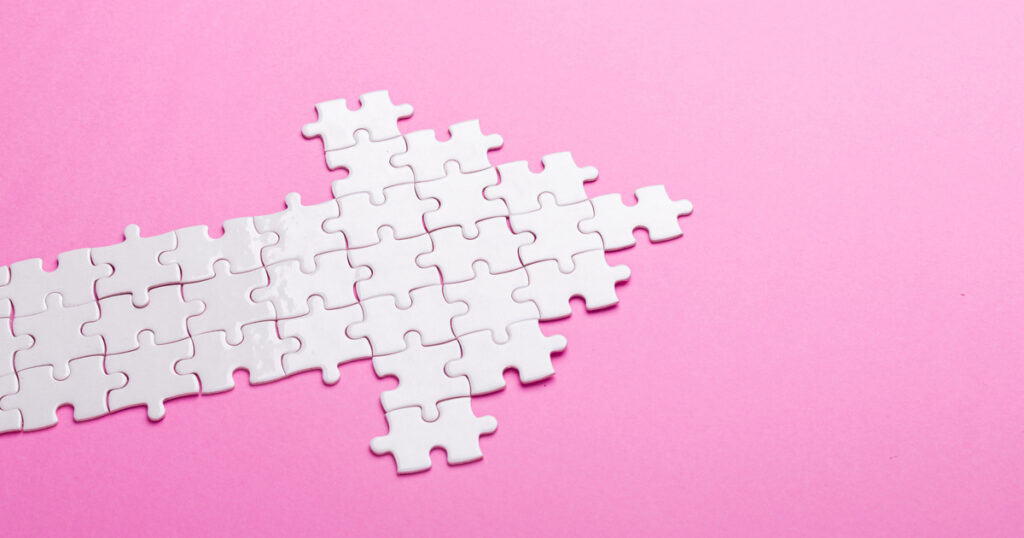Arrow made of white puzzle pieces on pink background.