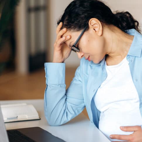 exhausted pregnant woman sitting at home office desk