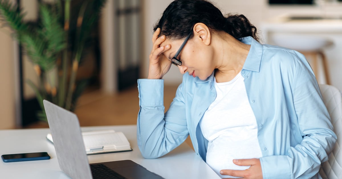 exhausted pregnant woman sitting at home office desk