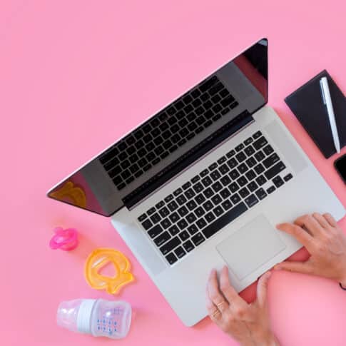 Working mom top view flatlay of workplace baby items and laptop with phone; work family concept