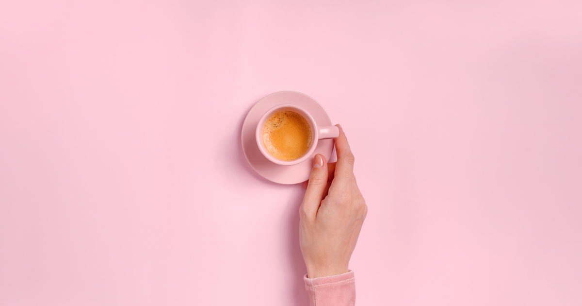 Hand holding pink coffee cup on pink background.