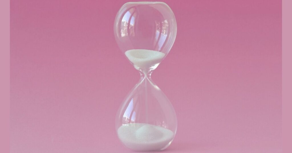 Glass hourglass on pink background