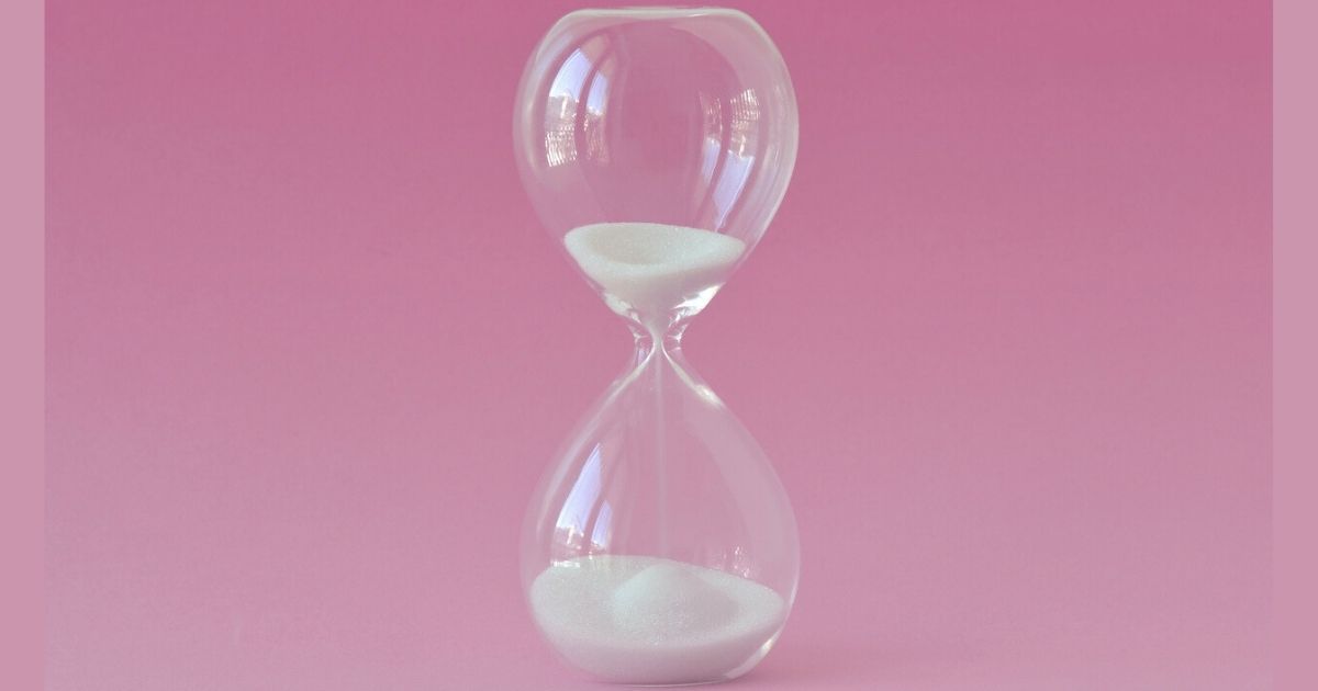 Glass hourglass on pink background