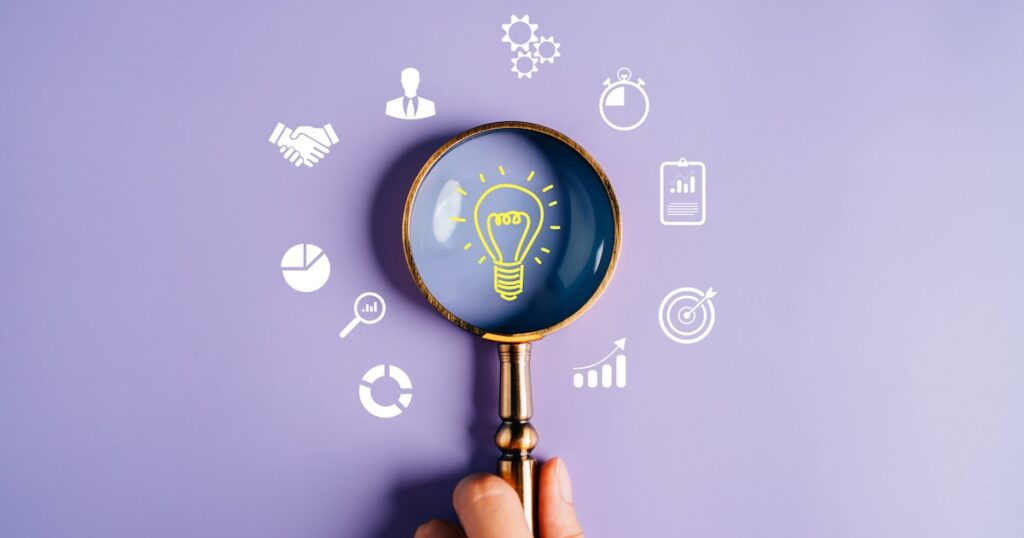 Magnifying glass highlights business icons on purple background.