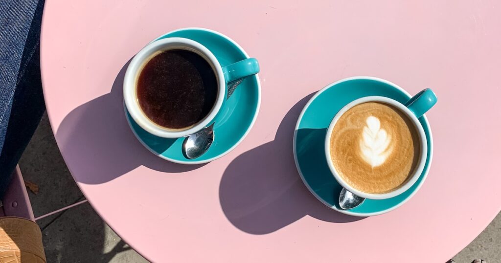 Two coffee cups on a pink table.