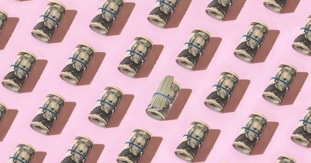 Pattern of rolled money on pink background.