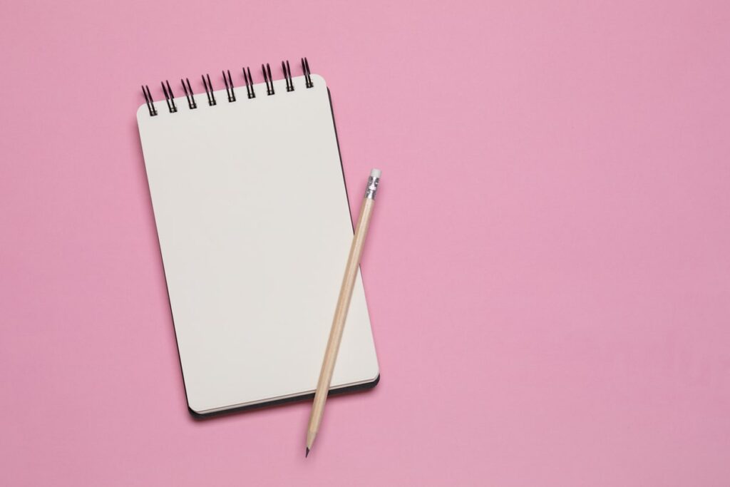 Spiral notebook and pencil isolated on pink background