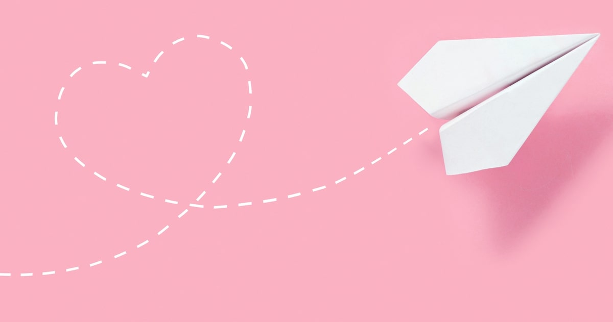 Paper airplane on pink background with heart shaped flight path
