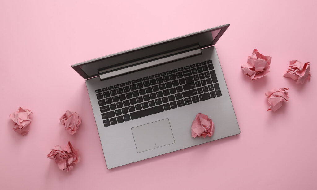 laptop surrounded by crumpled sheets of paper on pink background