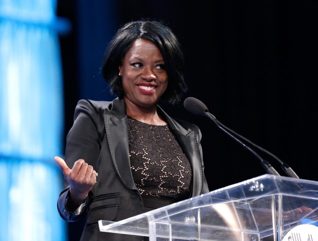 Viola Davis speaking at conference podium, smiling.