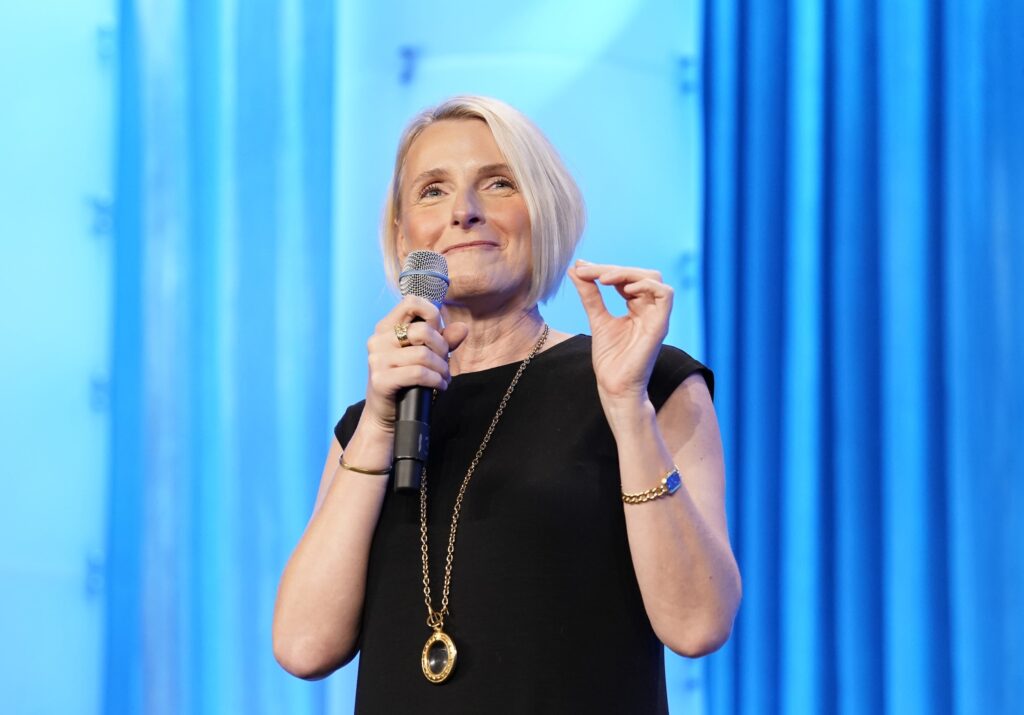 Woman speaking in front of blue curtain background.