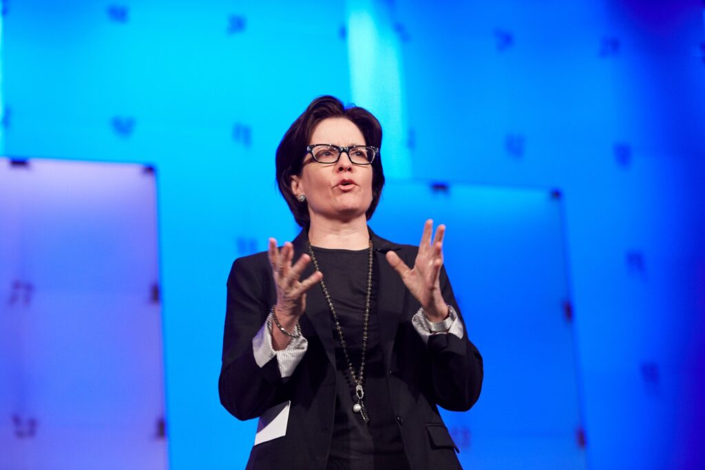 Person speaking on stage with blue background.
