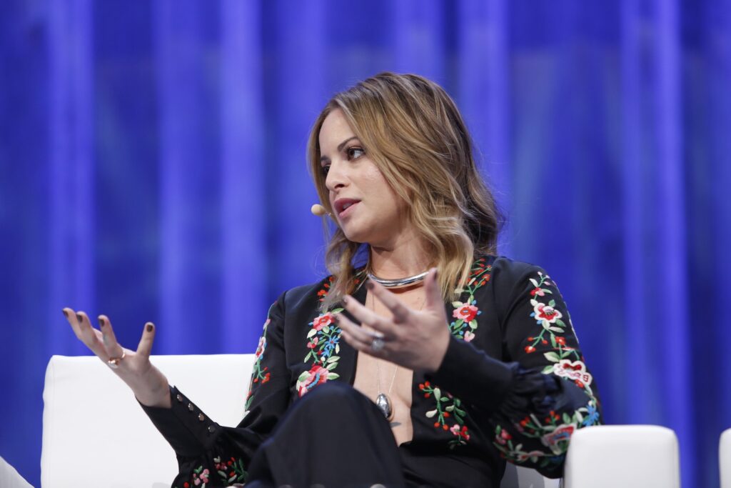 Person speaking on stage with blue background.