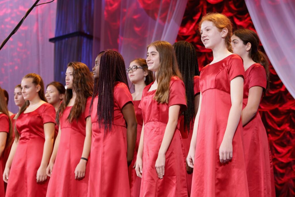 Girls' choir singing in red dresses on stage.