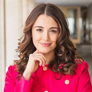 Smiling woman in red coat posing indoors.