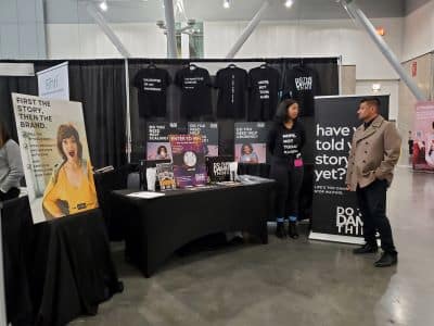 People talking at marketing booth with shirts and posters.