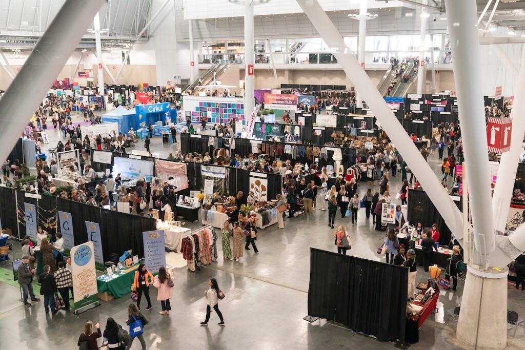 Crowded indoor trade show with vendor booths and attendees