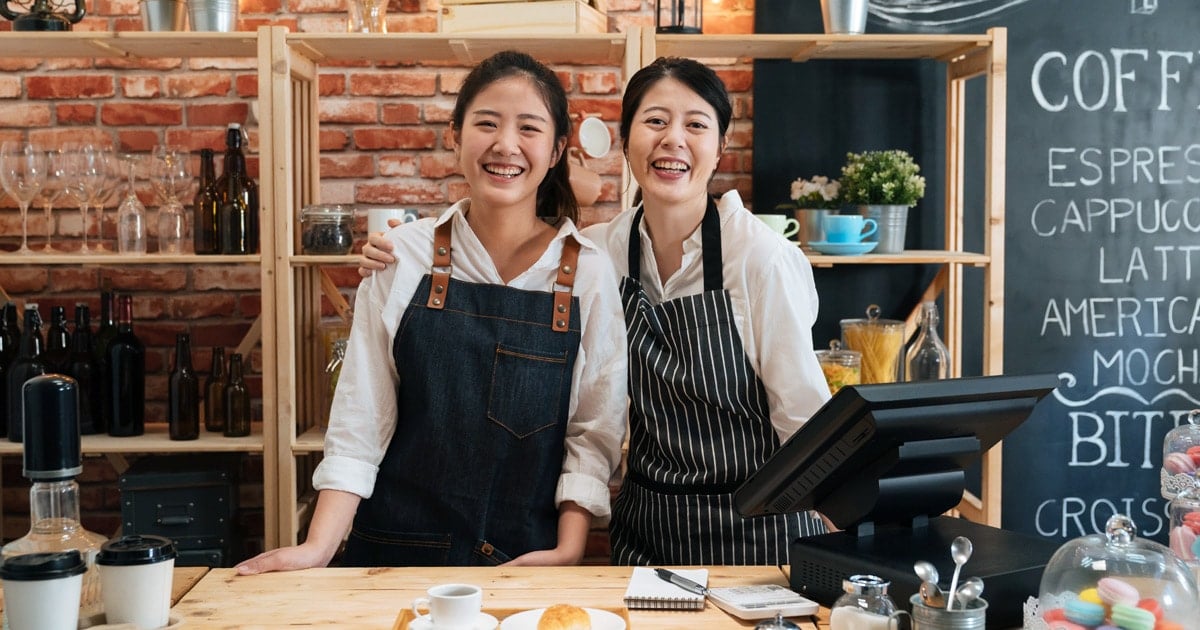 Smiling baristas standing behind coffee shop counter