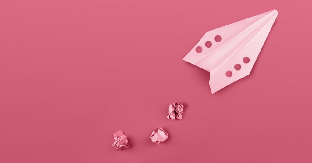 Flat lay of color paper plane colored in trendy color of the year 2023 Viva Magenta