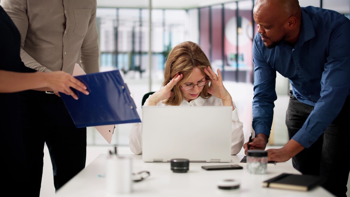 Stressed employee at laptop with colleagues assisting