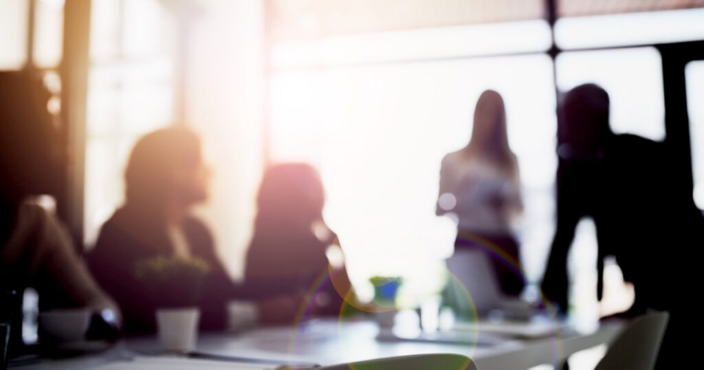 Sunlit silhouettes of coworkers in a blurred office meeting