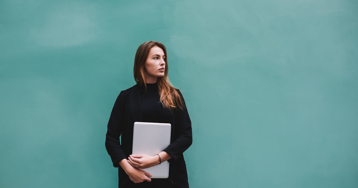 Woman holding laptop against a teal wall
