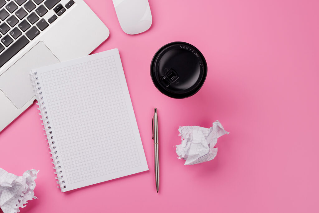 Pink desk with laptop, notebook, pen, and coffee