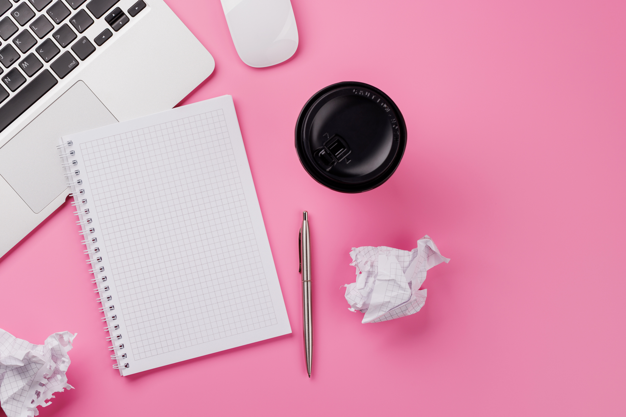 Pink desk with laptop, notebook, pen, and coffee